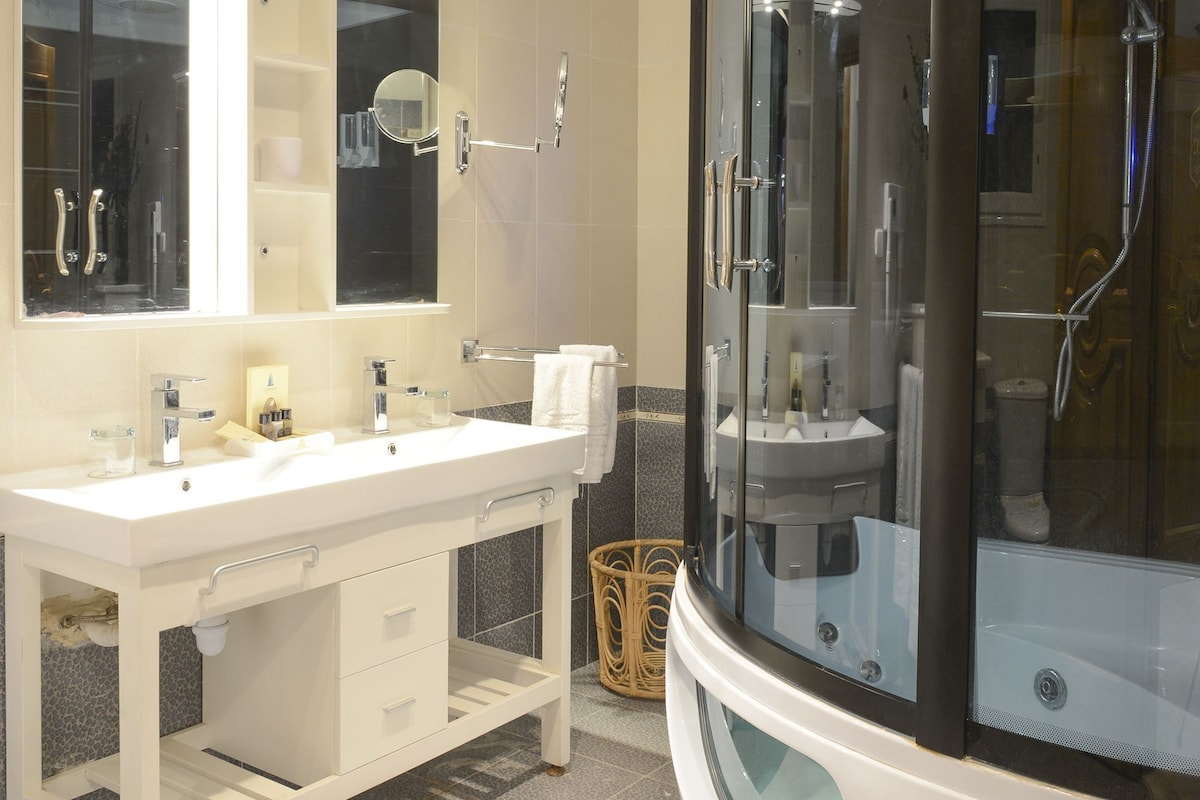 A modern bathroom with a large mirror, two sinks, a glass-enclosed shower, and a white vanity.