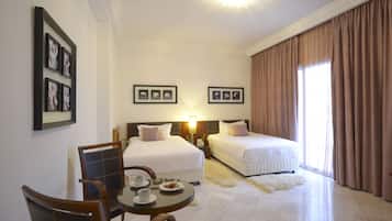 A hotel room with two beds, a dining table with chairs, and framed pictures on the wall.
