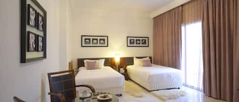 Une chambre d’hôtel avec deux lits, une table à manger avec des chaises et des tableaux encadrés au mur.