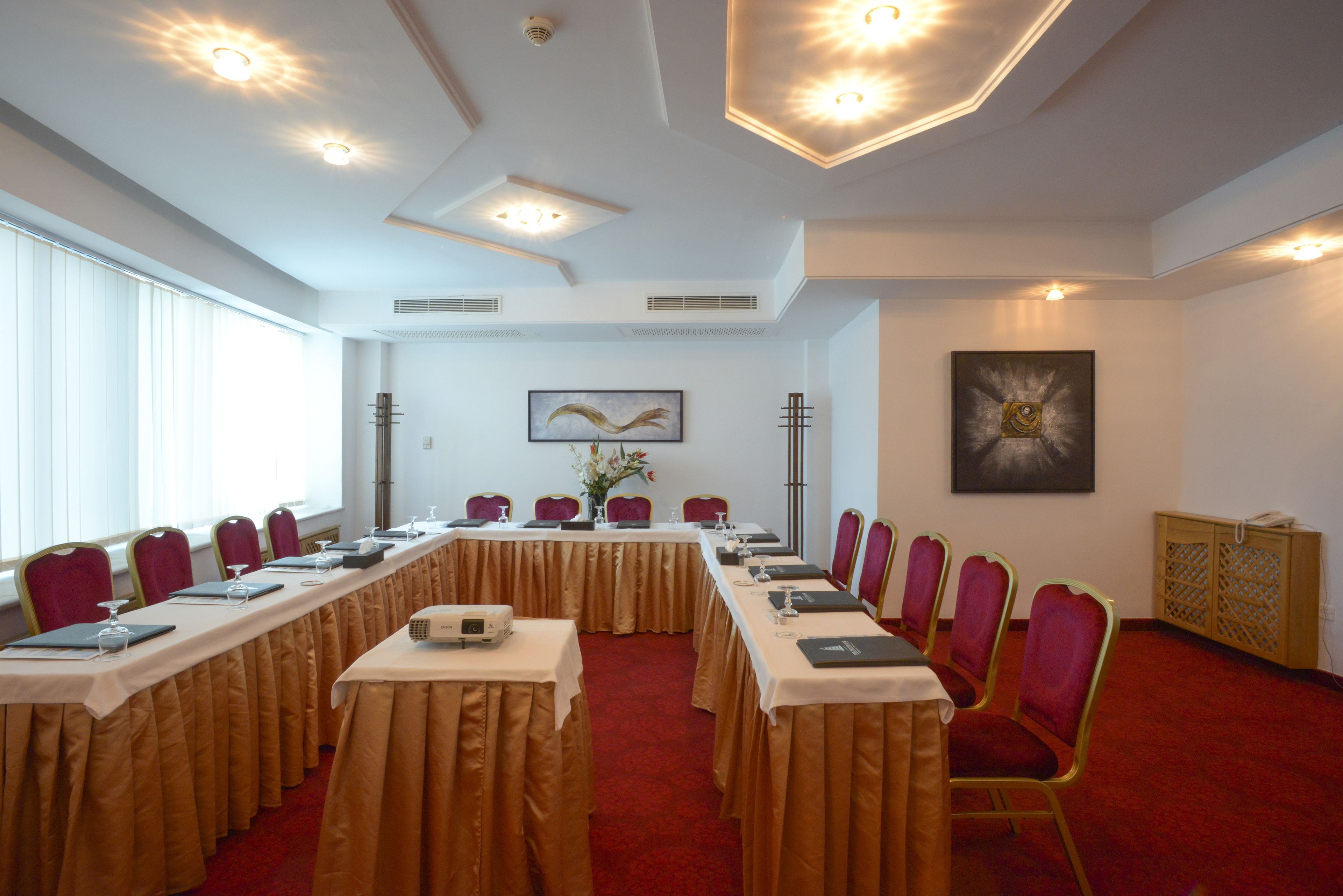 Una sala conferenze con lunghe tavole, sedie rosse e un tappeto rosso.