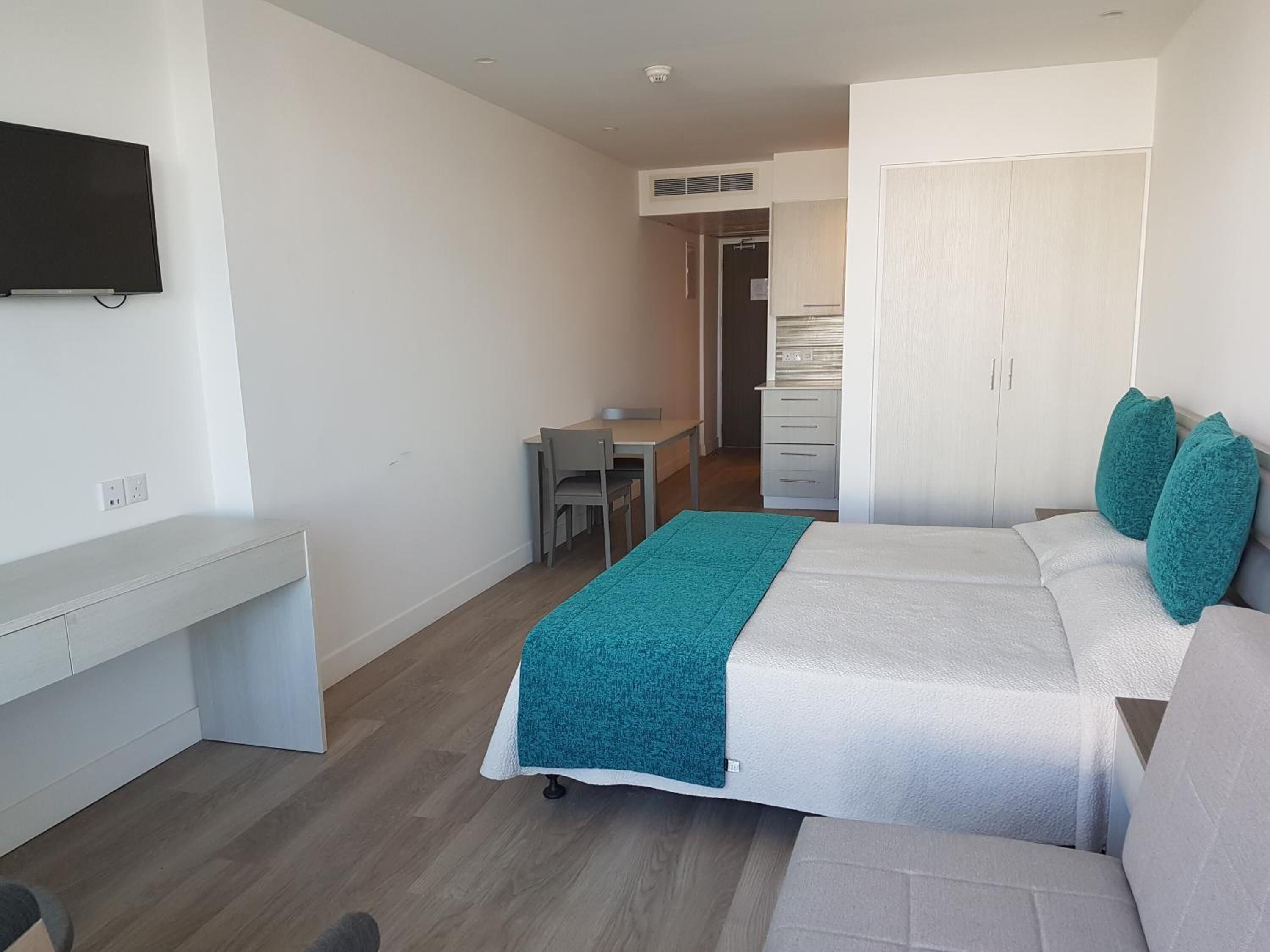 A modern hotel room with a bed, a desk, a chair, and a television.