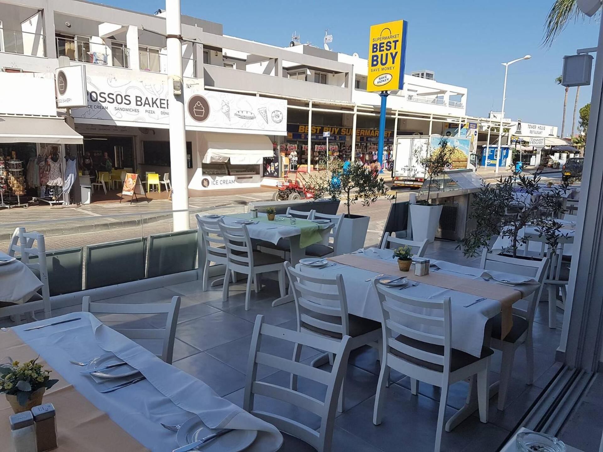 An outdoor dining area with tables and chairs, a sign for 'Best Buy' supermarket, and a building with 'POSSOS BAKE' signage.
