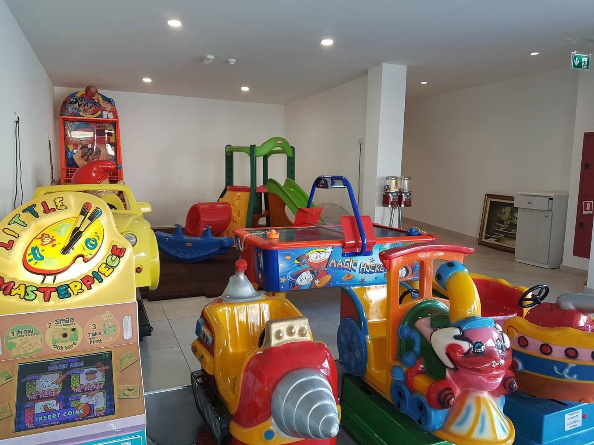 Un área de juegos infantiles con diversos vehículos de juguete coloridos y un fotomatón.