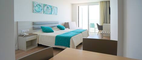 A modern hotel room with a bed, bedside table, and a desk with a chair. There is a balcony with a chair and a view of the outside.