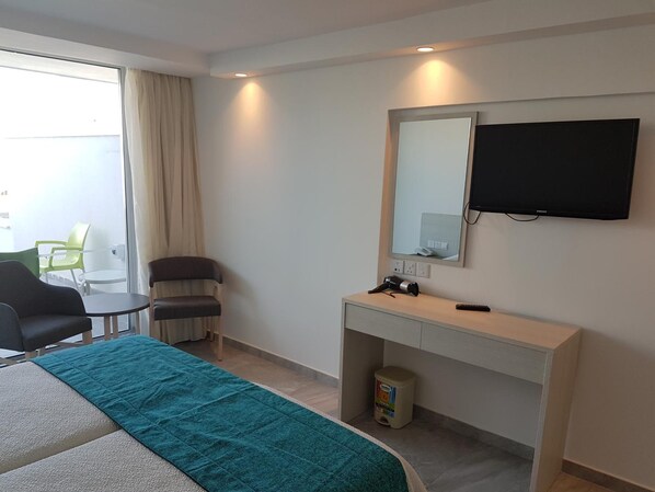 A hotel room with a bed, a desk, a chair, a TV, and a window with curtains. - Melini Hotel Suites (Paralimni)