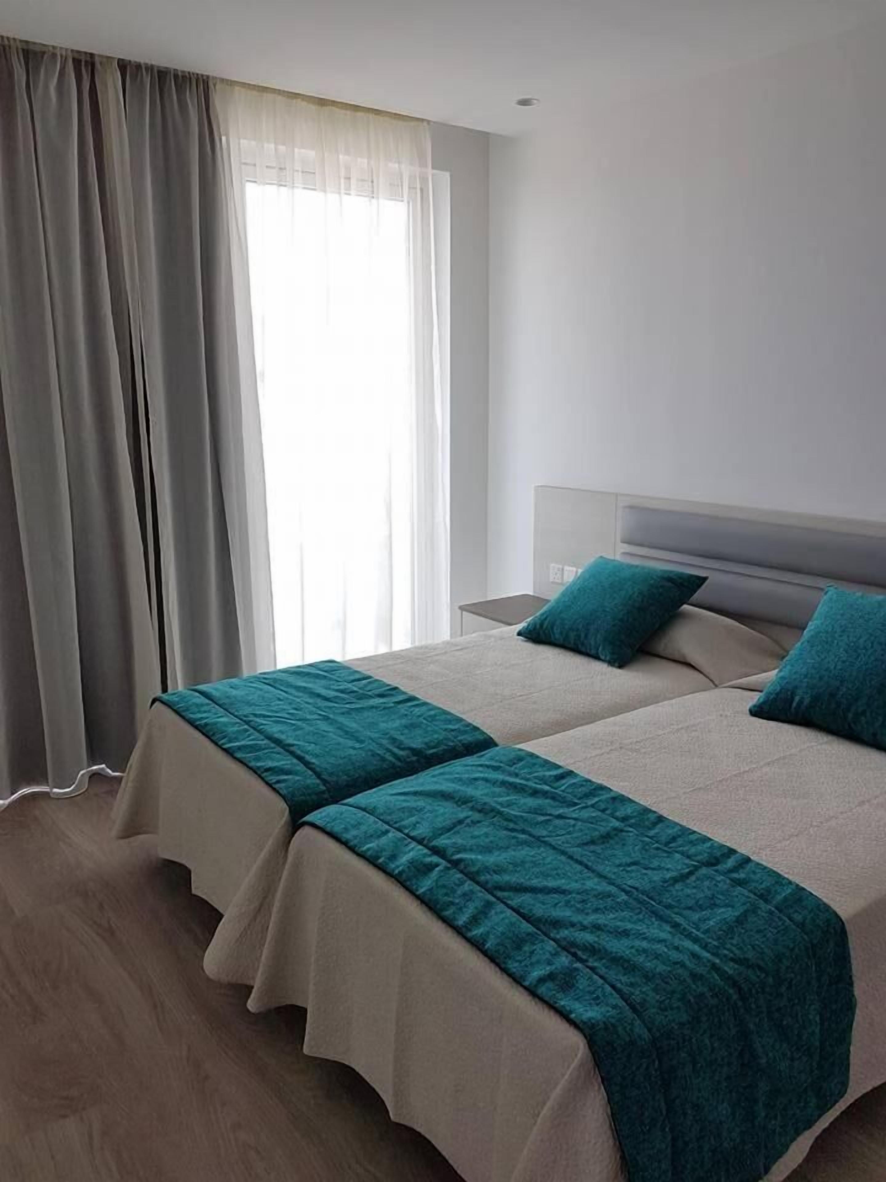 A hotel room with two beds, a large window with sheer curtains, and a wooden floor.