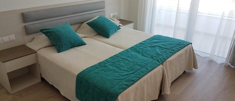 A double bed with a beige headboard and two pillows, a green throw blanket, and a nightstand with a lamp.