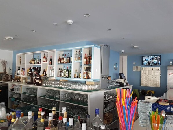 A bar area with shelves of liquor bottles, glasses, and a refrigerator.