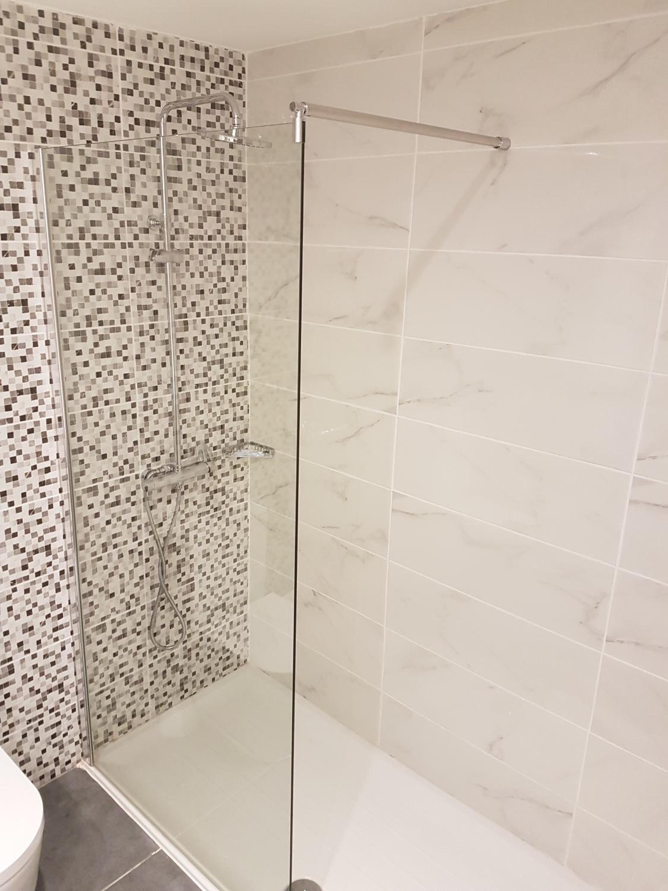Une douche avec une porte en verre, un mur carrelé orné d’un motif en mosaïque et un sol en marbre.
