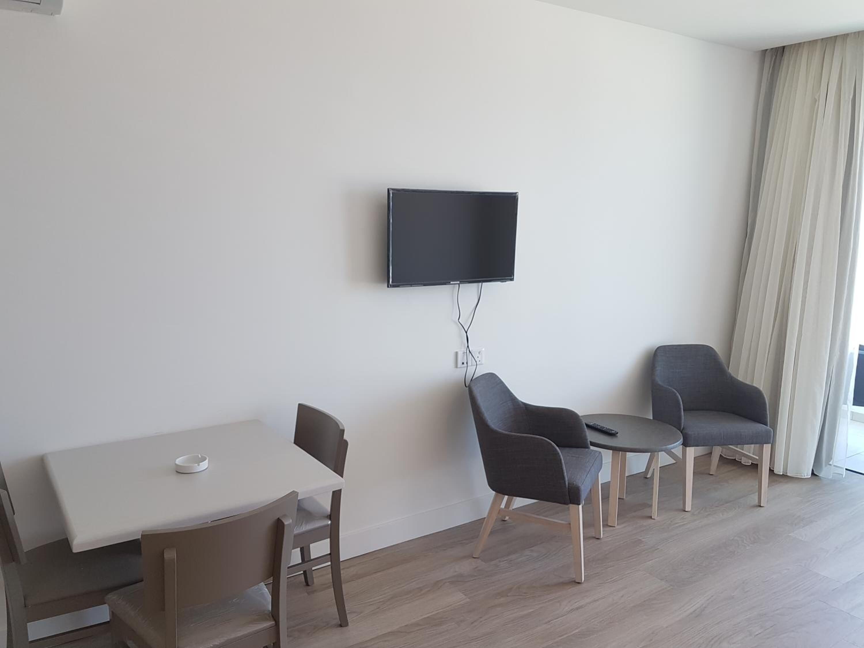 Un salon moderne avec un téléviseur à écran plat fixé au mur, une table à manger avec des chaises et une petite table d’appoint.