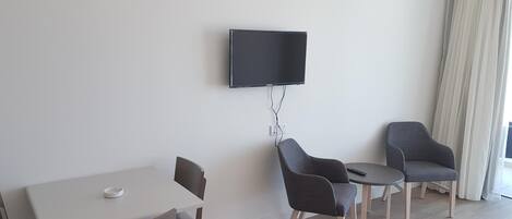 Un salon moderne avec un téléviseur à écran plat fixé au mur, une table à manger avec des chaises et une petite table d’appoint.