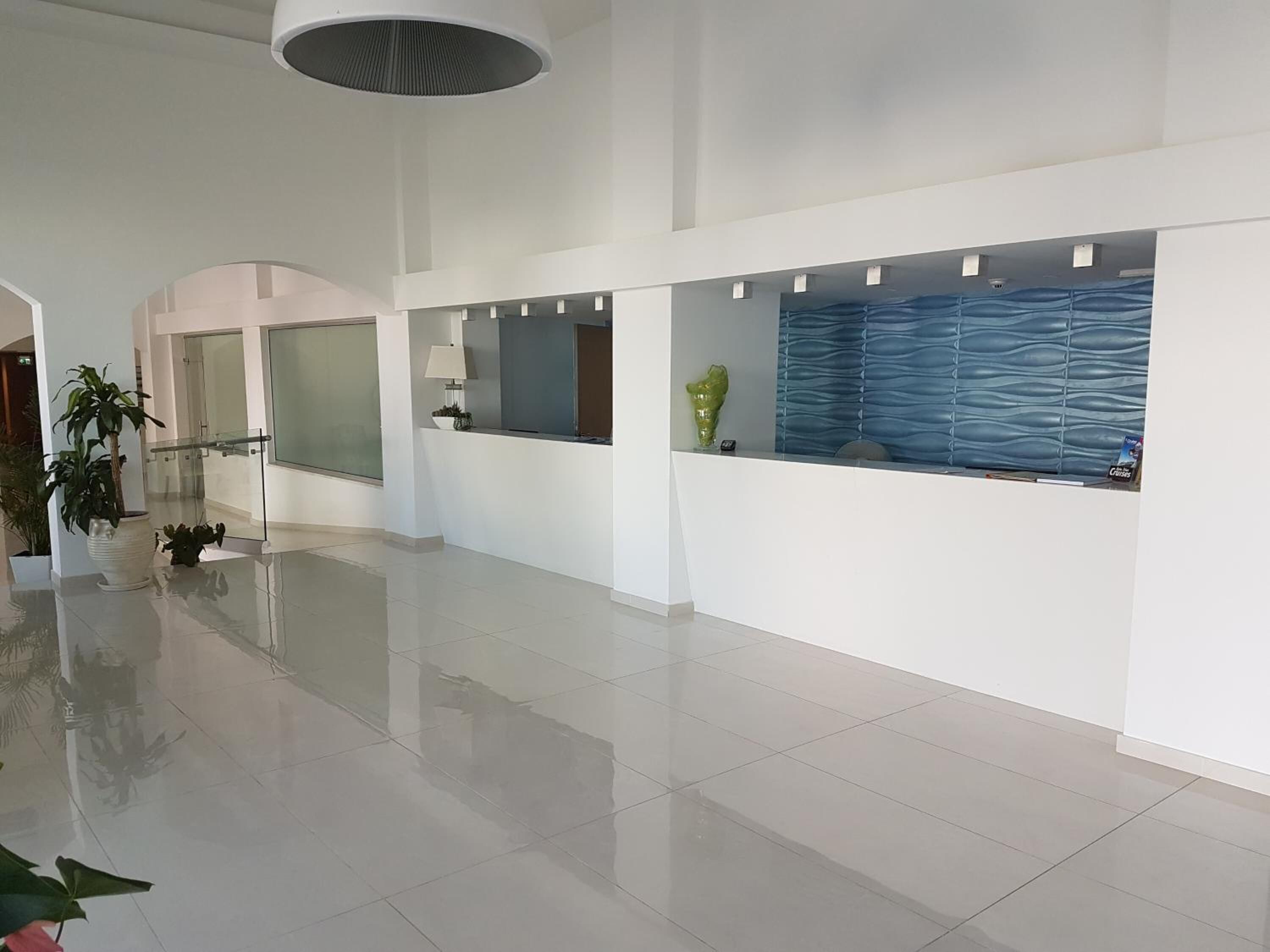 A spacious lobby with a high ceiling, a reception desk, and a large window with a blue patterned blind.