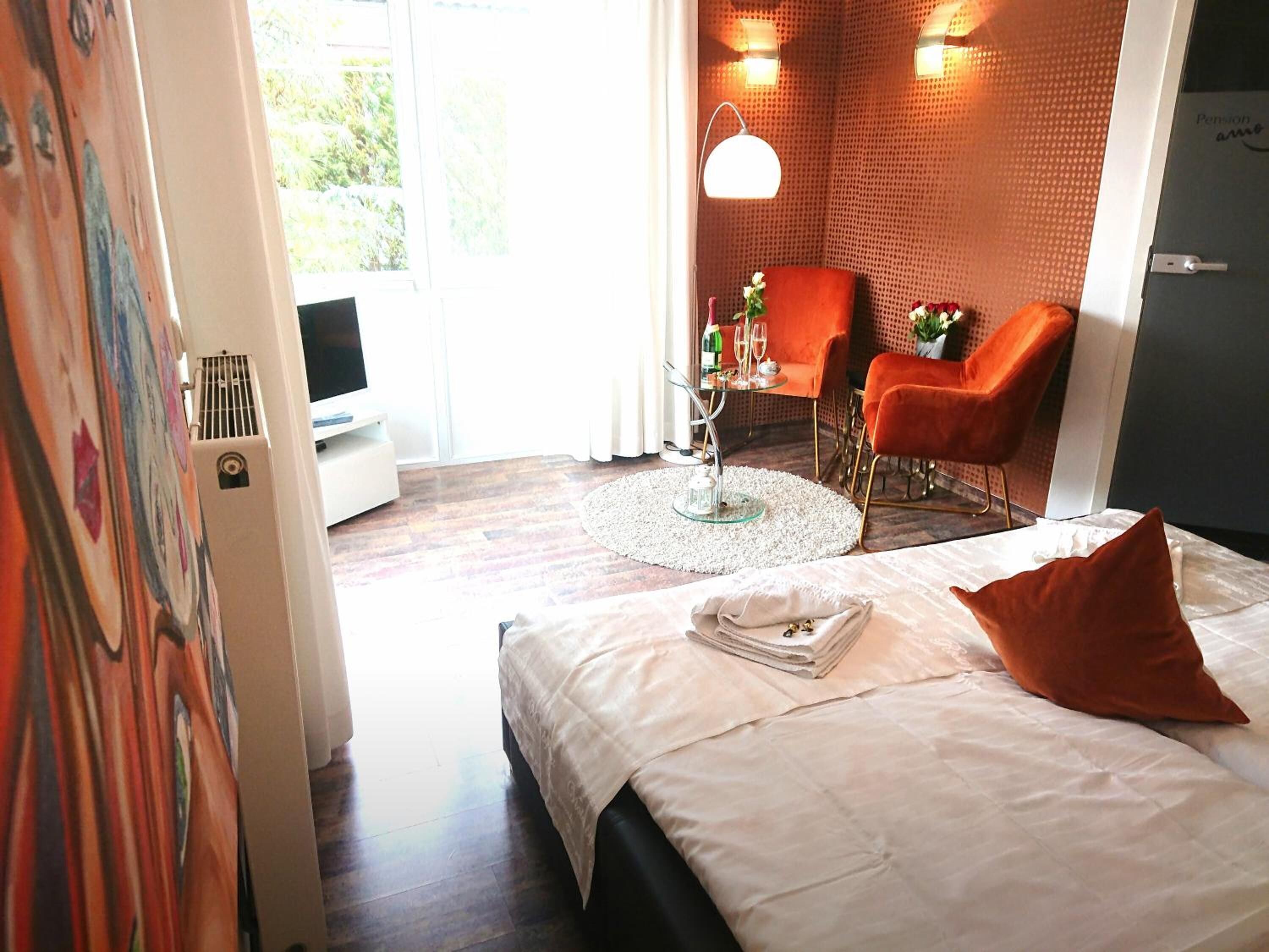 Une chambre d’hôtel avec un lit, un bureau, deux chaises, une petite table avec un vase et une fenêtre avec des rideaux.