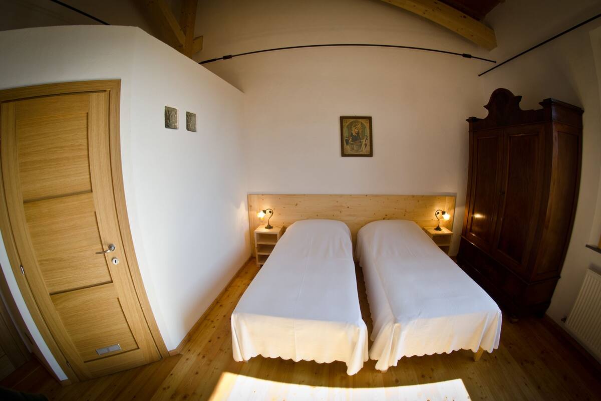 A room with two single beds, a wooden wardrobe, a small bedside table with a lamp, and a door.