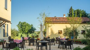 An outdoor seating area with tables and chairs, surrounded by greenery and a building with a tiled roof. - Agriturismo Campanacci (Faenza)