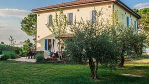 A two-story building with a tiled roof, a balcony, and a garden area with a tree and outdoor seating. - Agriturismo Campanacci (Faenza)