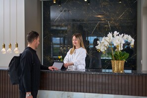 A reception desk with a receptionist, a man, and a potted orchid. - Hotel Filippos (Chalkidona)