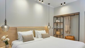 A neatly made bed with white linens and beige pillows, a bedside table with a vase of flowers, and a hanging lamp. - Hotel Filippos (Chalkidona)
