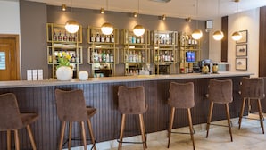 A bar area with a wooden counter, multiple stools, and shelves stocked with bottles. - Hotel Filippos (Chalkidona)