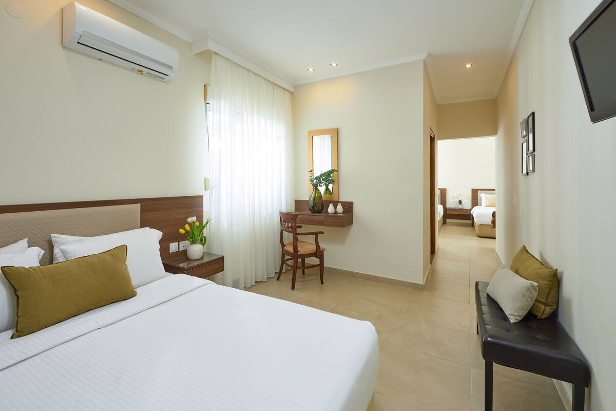 A hotel room with a large bed, a bedside table with a vase of flowers, a chair, and a small desk with a mirror.