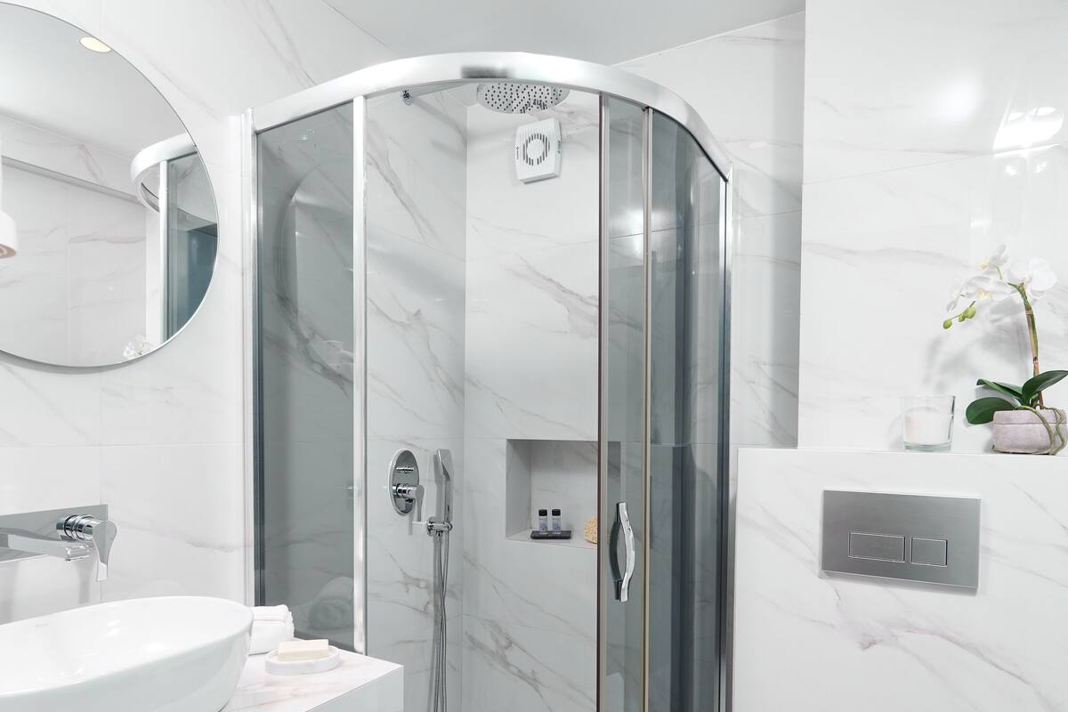 A modern bathroom with a glass-enclosed shower, a round mirror, a white sink, and a toilet.