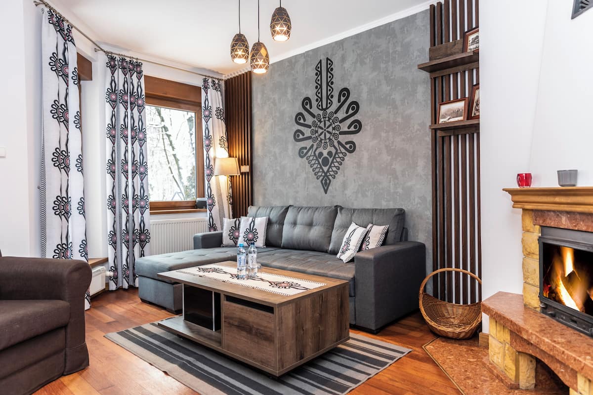 Una sala de estar con sofá, mesa de centro, chimenea y cortinas estampadas.