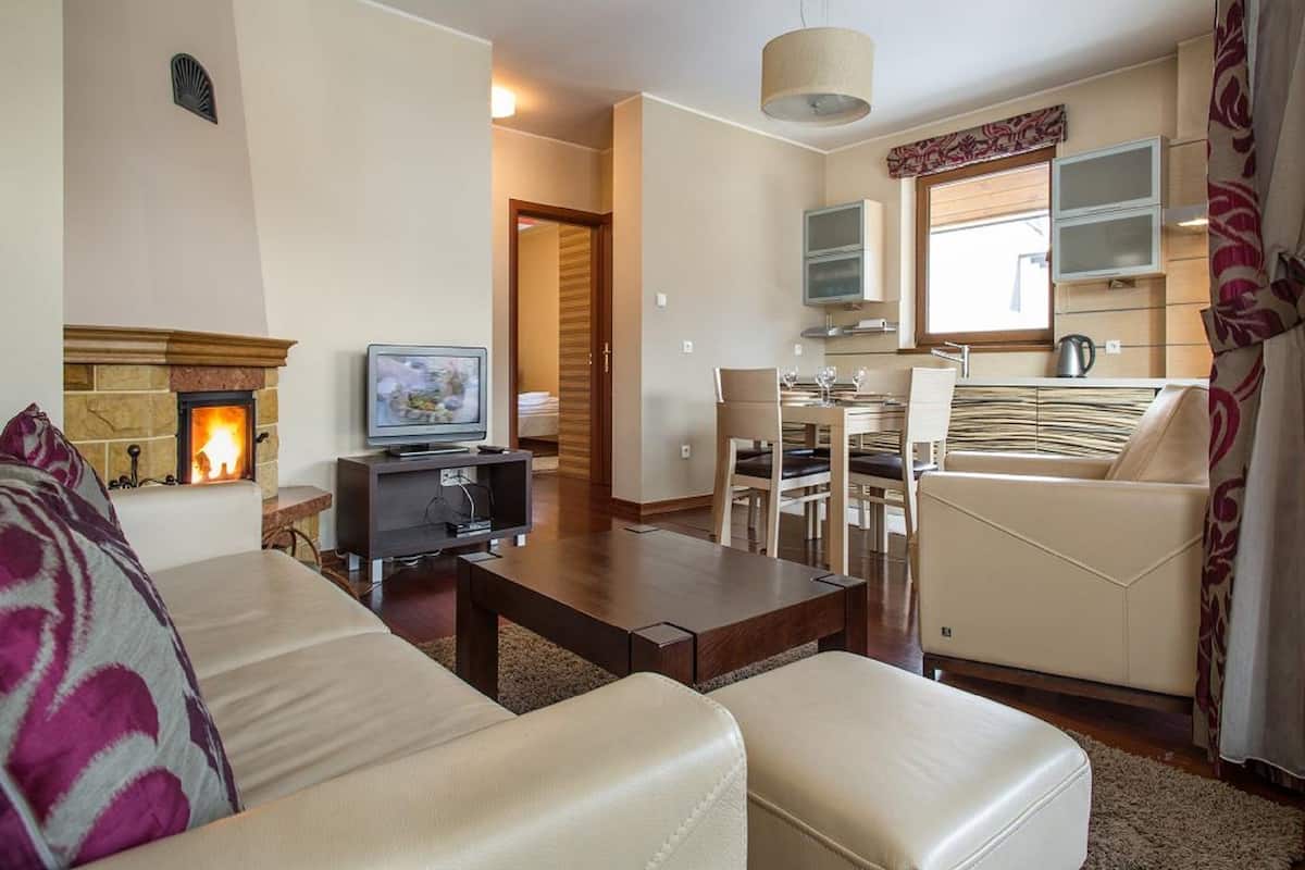 Una sala de estar con chimenea, televisor, comedor con mesa y sillas, y área de cocina con ventana.