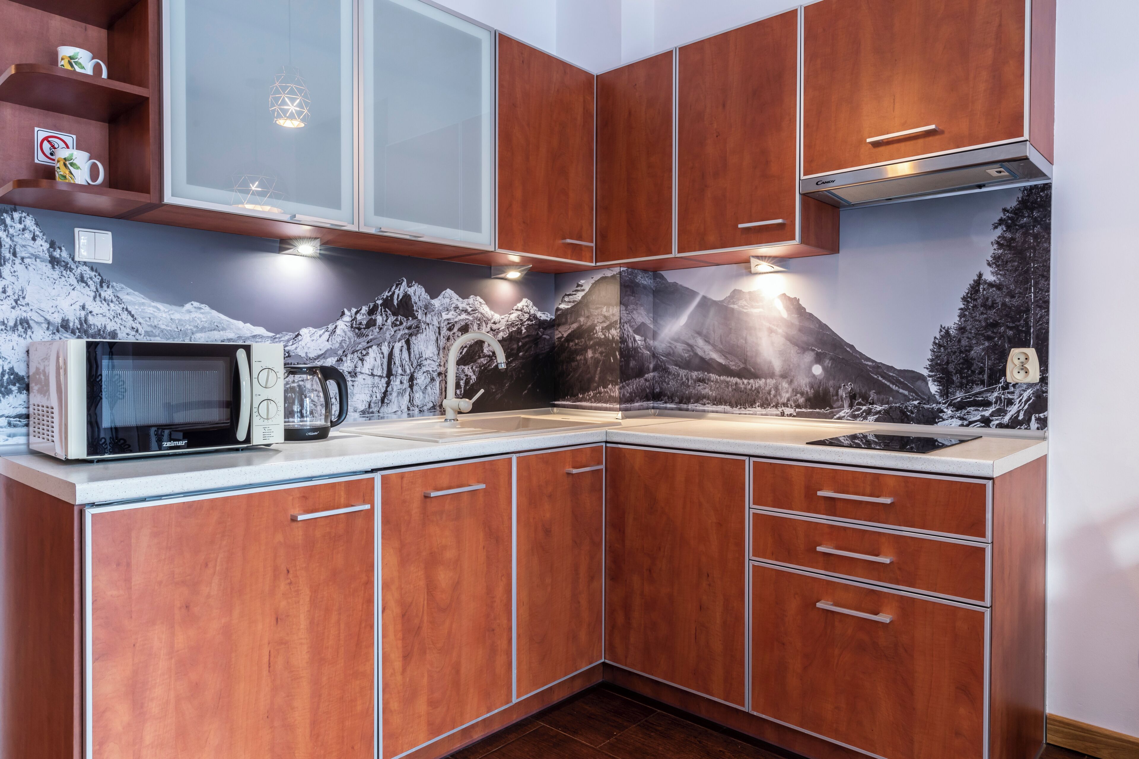 Una cocina con armarios de madera, microondas y un mural con motivos de montaña.