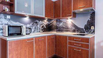 Una cocina con armarios de madera, microondas y un mural con motivos de montaña.