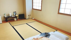 Une pièce avec un sol recouvert de tatamis, comprenant un lit, une petite table avec une lampe et un téléviseur.