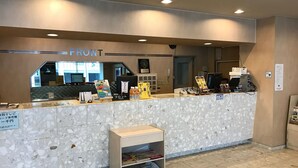 Un comptoir d’accueil avec un revêtement en marbre, une petite étagère avec des magazines et un panneau indiquant le prix des services.