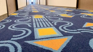 Un couloir d’hôtel avec un tapis à motifs, des portes de part et d’autre, et une lumière au bout.