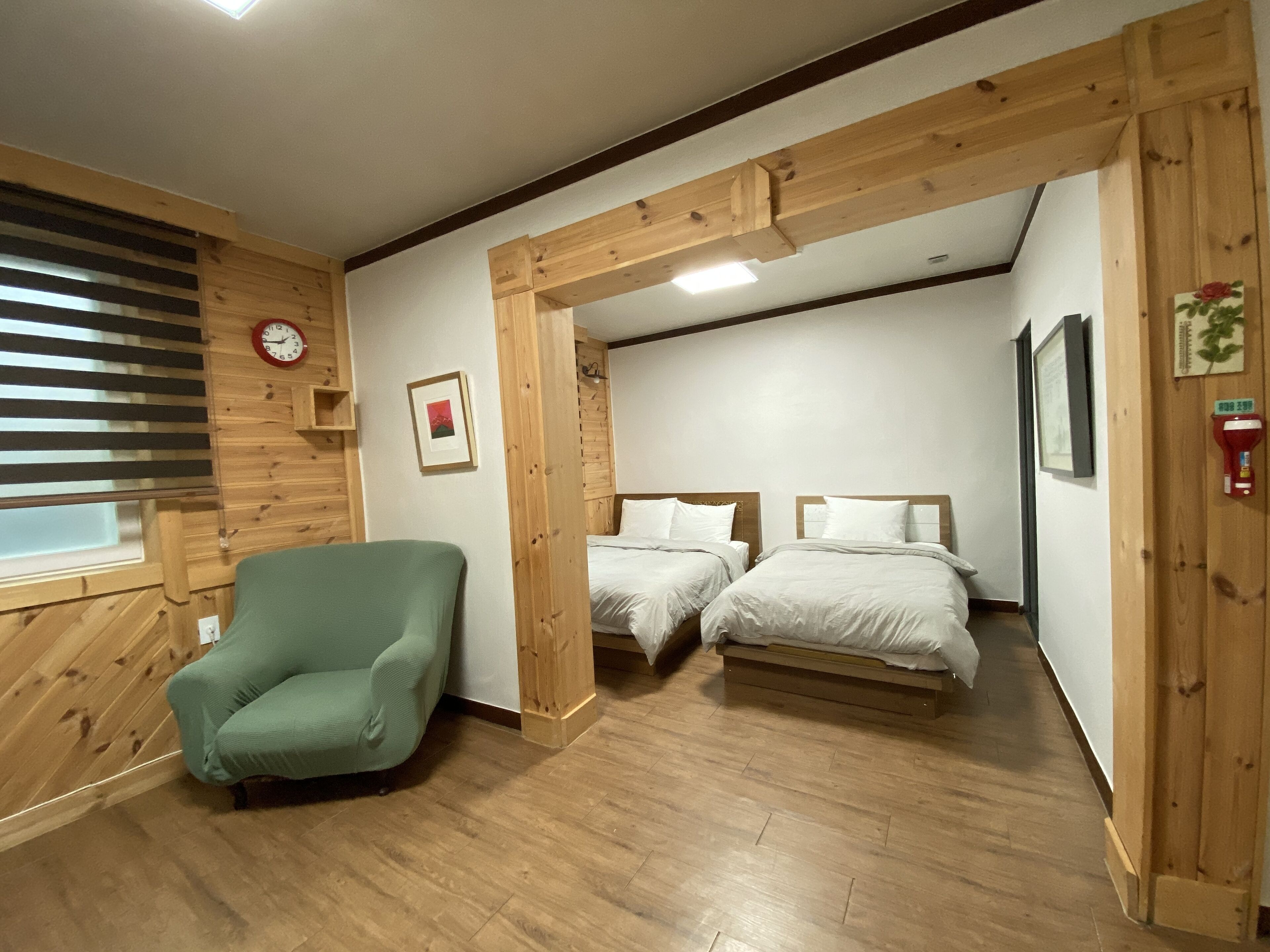 Ein Zimmer mit Holzbalken, zwei Betten, einem grünen Sessel, einer Uhr und einem gerahmten Bild an der Wand.