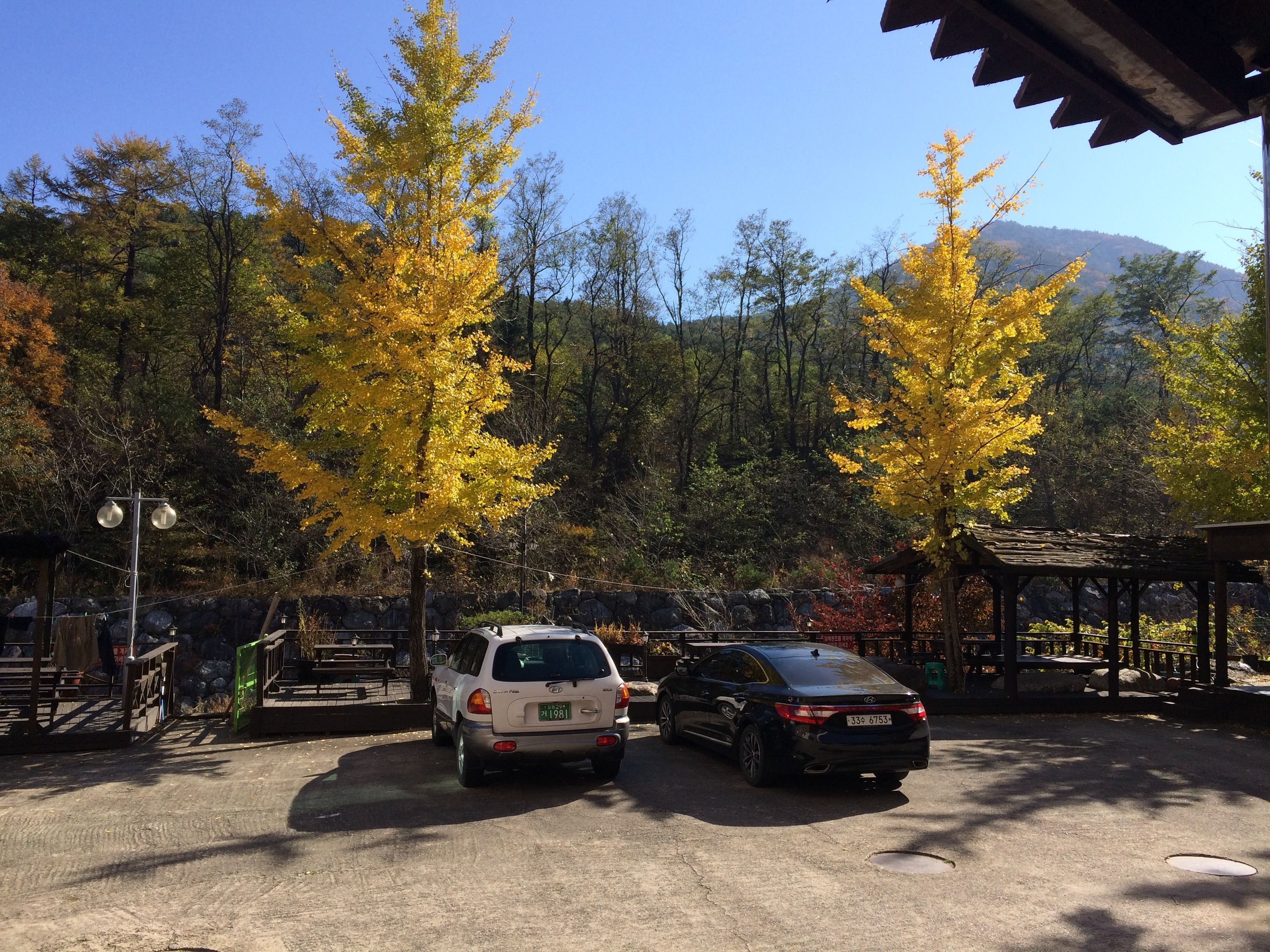 A parking area with two cars, a gazebo, and a stone wall.