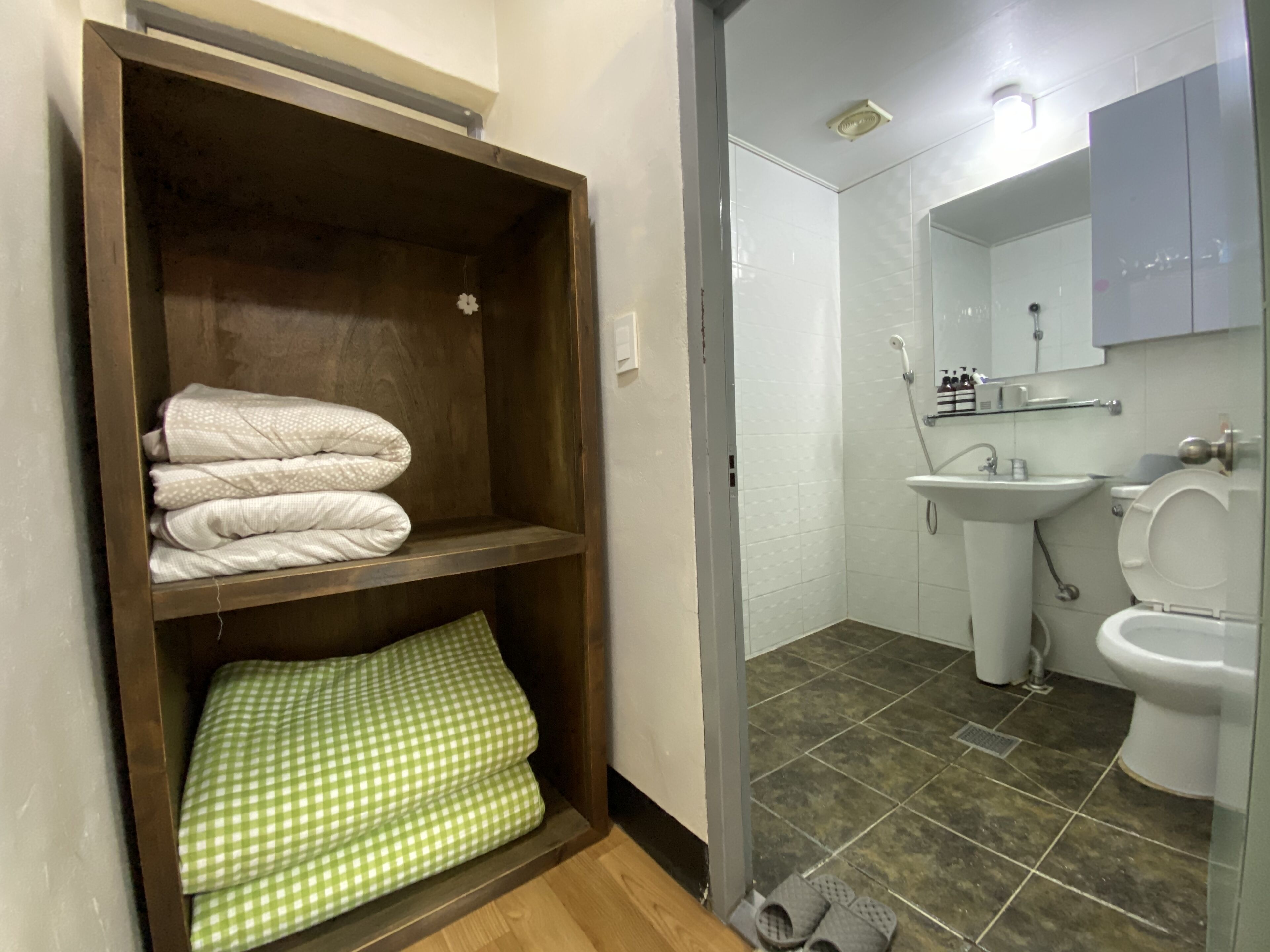 Ein Badezimmer mit Holzregal, darauf gefaltete Handtücher, einem Waschbecken und einer Toilette.