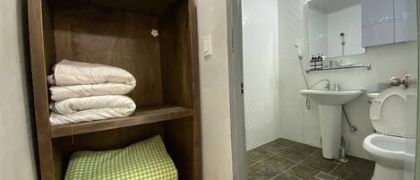 Ein Badezimmer mit Holzregal, darauf gefaltete Handtücher, einem Waschbecken und einer Toilette.