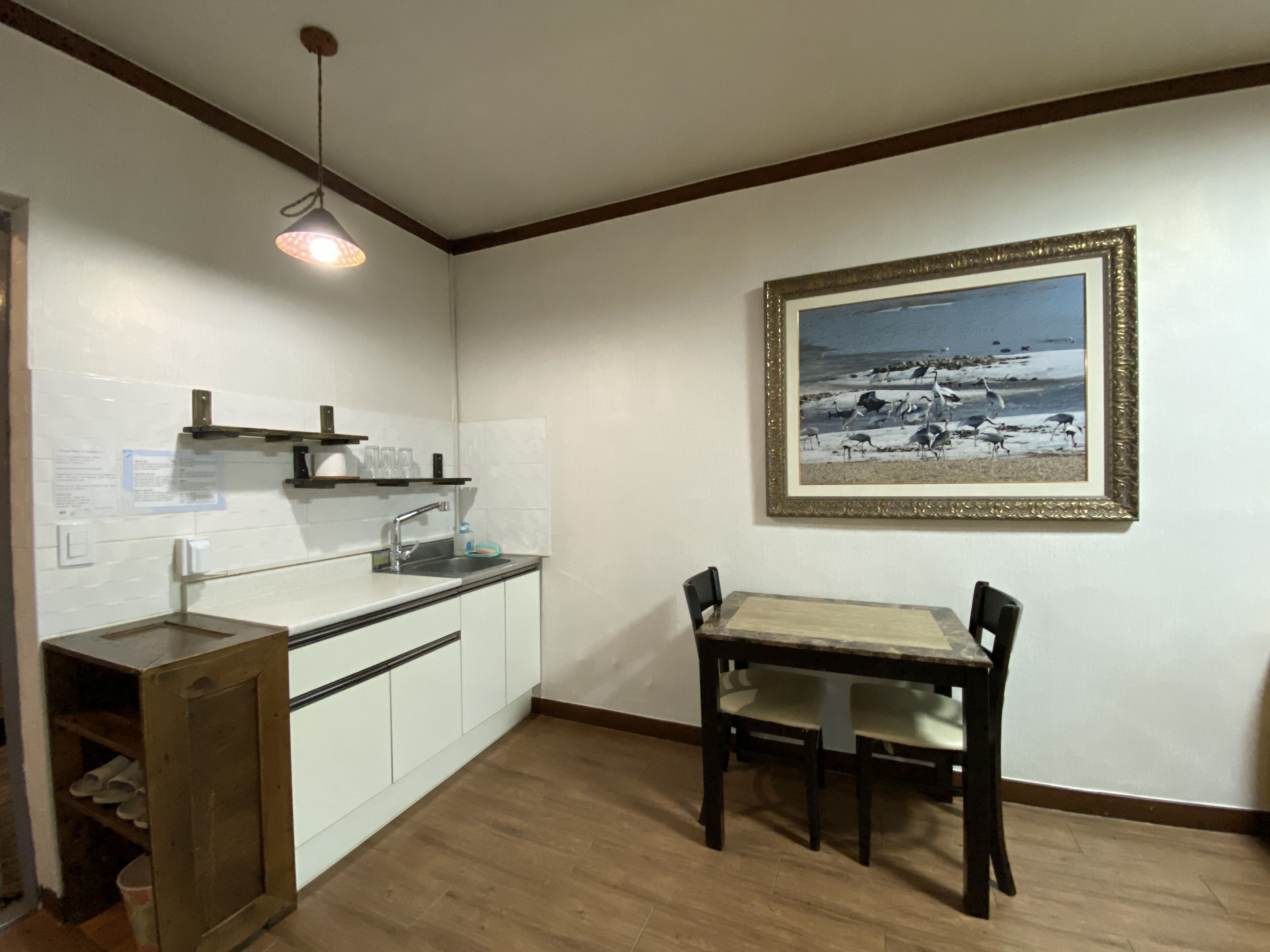 A kitchen with white cabinets, a sink, and a wooden table with chairs. There is a framed picture on the wall.