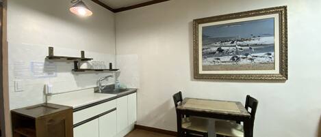 A kitchen with white cabinets, a sink, and a wooden table with chairs. There is a framed picture on the wall.