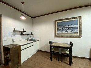 A kitchen with white cabinets, a sink, and a wooden table with chairs. There is a framed picture on the wall. - Smile Resort (Sokcho)