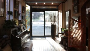 A cozy interior with a piano, wooden flooring, and a large window with a view of the street.