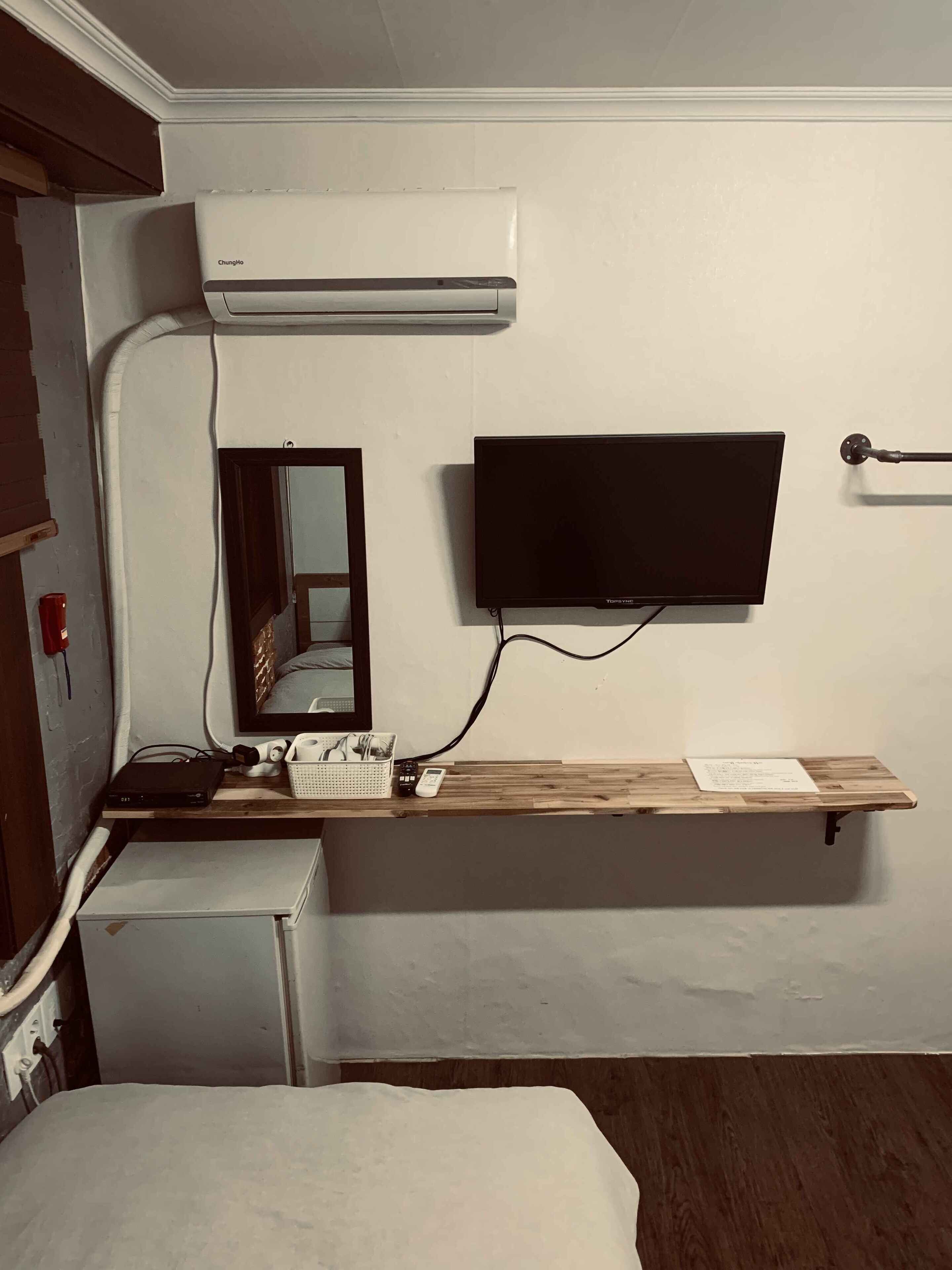 Une chambre d’hôtel équipée d’un lit, d’un bureau avec un téléviseur à écran plat, d’un miroir et d’un climatiseur fixé au mur.