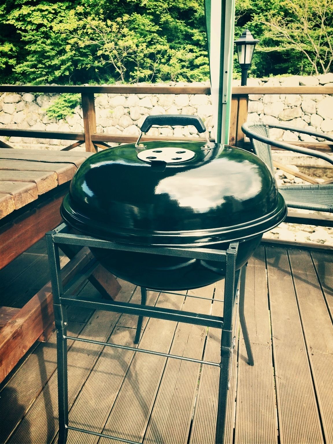 Un barbecue noir, posé sur un support métallique, sur une terrasse en bois.