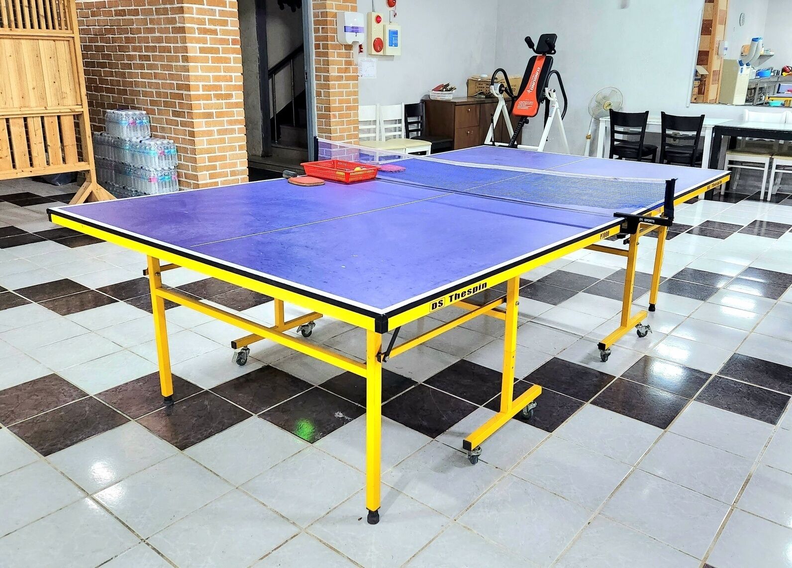 Et ping pong-bord på hjul i et rum med skakternet gulv.