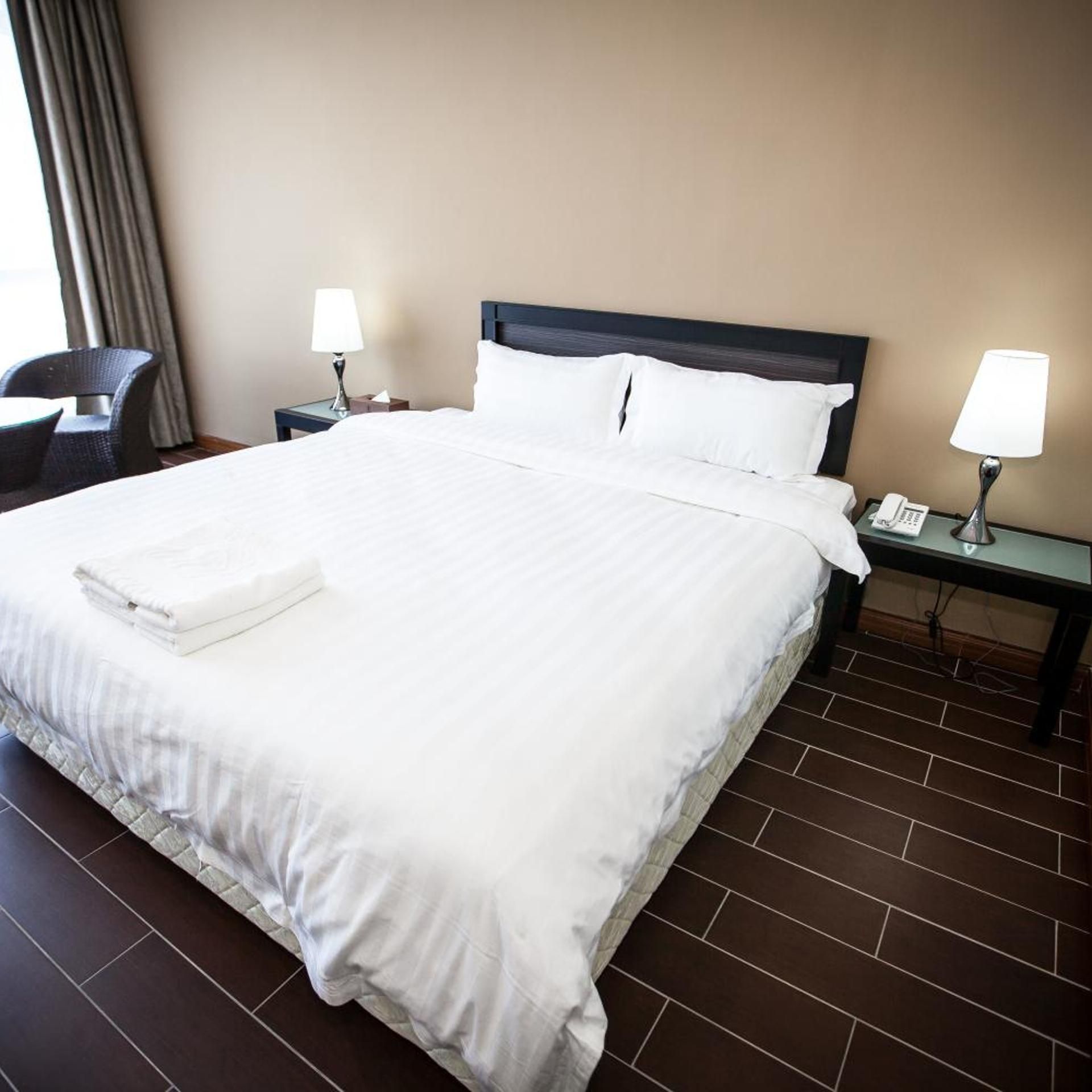 A hotel room with a large bed, two bedside tables with lamps, a chair, and a window with curtains.