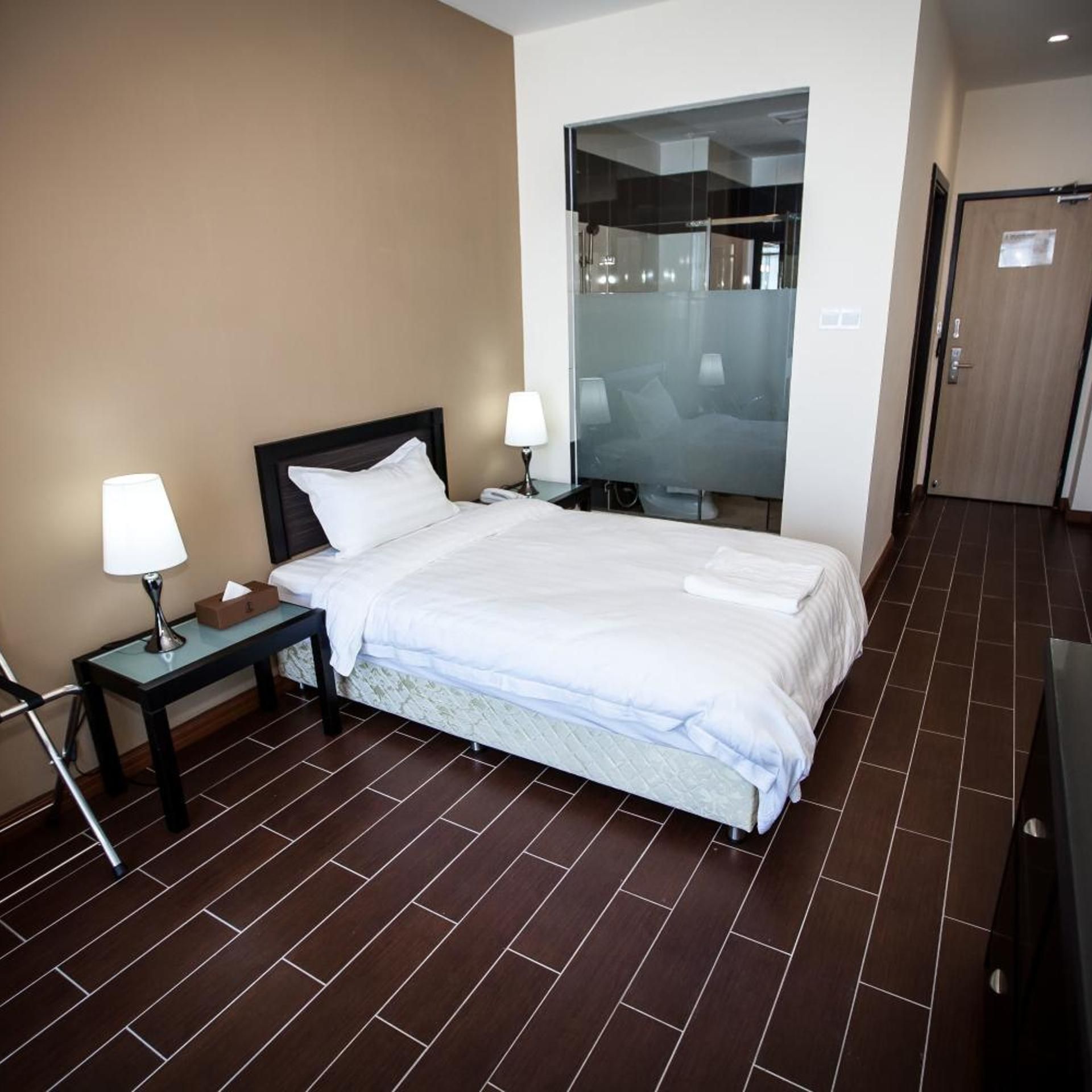 A hotel room with a bed, bedside tables with lamps, a mirror, and a door.