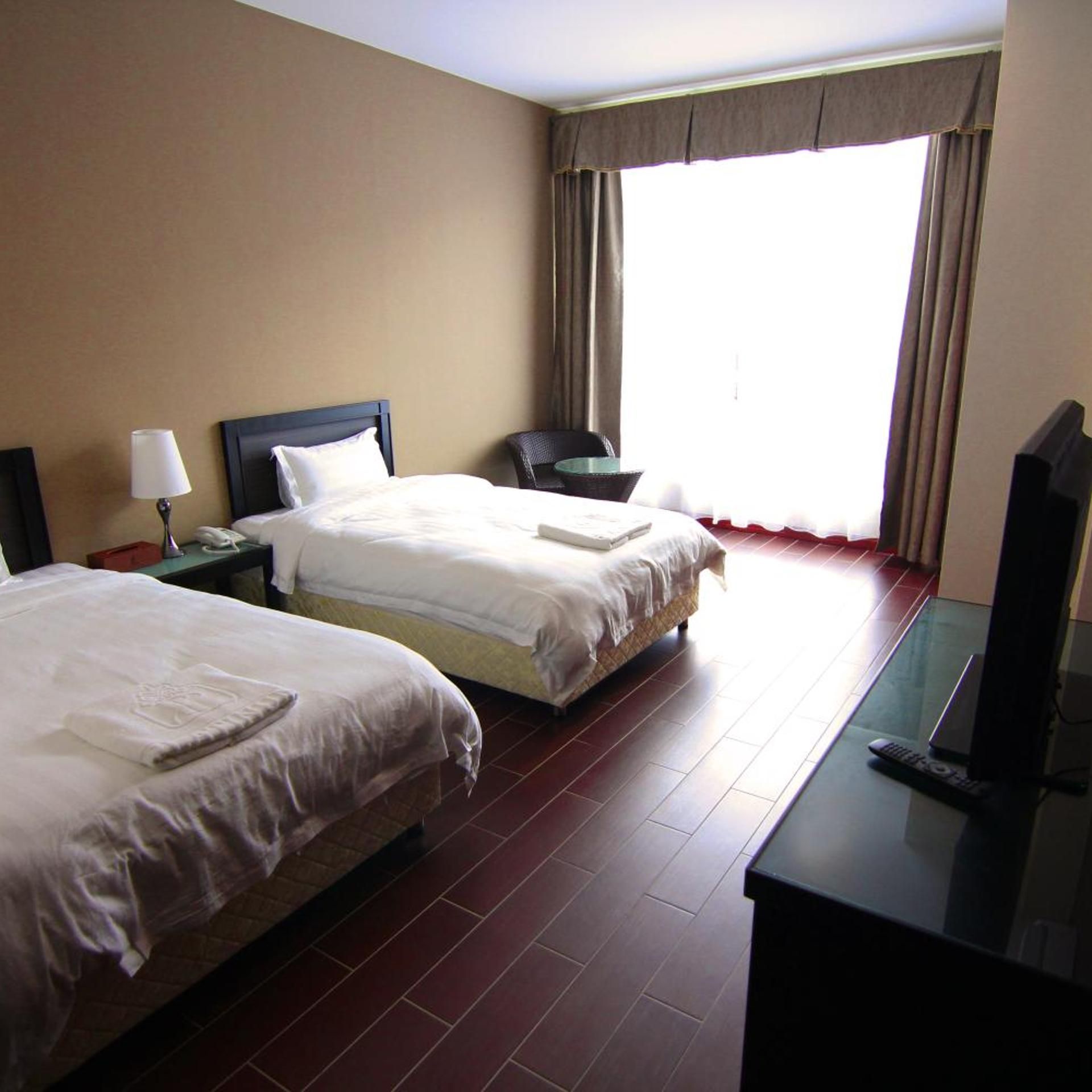 Habitación de hotel con dos camas, un escritorio con televisor y una ventana con cortinas.