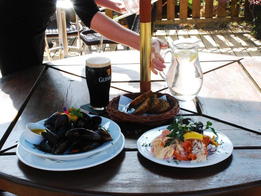 Una mesa con un plato de mejillones, una ensalada, una cerveza en un vaso y una jarra de agua.
