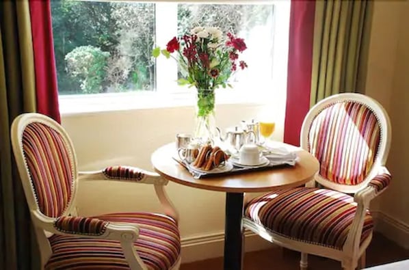 Un comedor con dos sillas a rayas, una mesa redonda con un jarrón de flores y una ventana con cortinas.