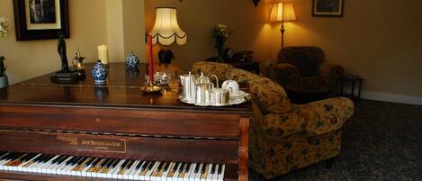 Un piano de cola, un sofá floral y una lámpara en una habitación acogedora con alfombra estampada.