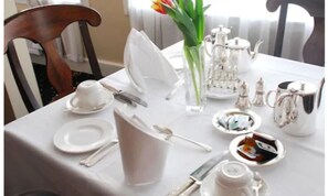 A table set for dining with white tablecloth, silverware, plates, a pitcher, a vase with flowers, and a teapot. - Casey's Hotel Glengarriff (Glengarriff)